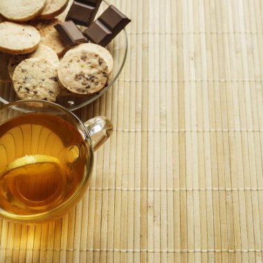 Cam bardak çay bisküvi ve hafif ahşap arka plan üzerinde limon ile. Çay limon ve bisküvi