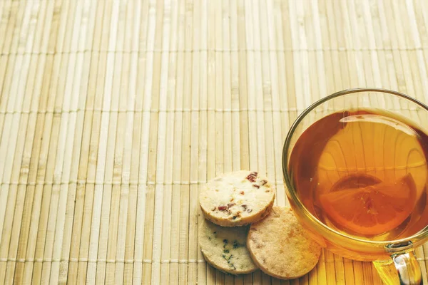 Cam bardak çay bisküvi ve hafif ahşap arka plan üzerinde limon ile. Çay limon ve bisküvi