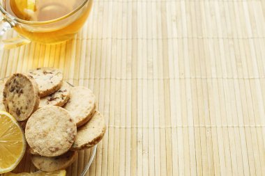 Cam bardak çay bisküvi ve hafif ahşap arka plan üzerinde limon ile. Çay limon ve bisküvi