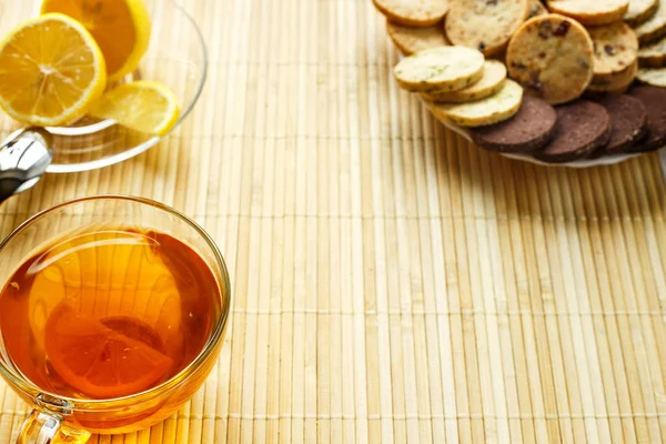 Cam bardak çay bisküvi ve hafif ahşap arka plan üzerinde limon ile. Çay limon ve bisküvi