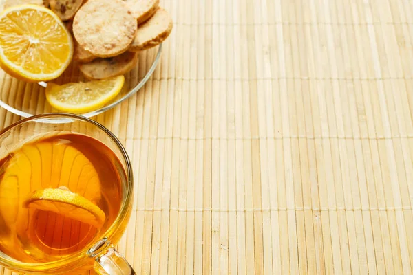 Cam bardak çay bisküvi ve hafif ahşap arka plan üzerinde limon ile. Çay limon ve bisküvi