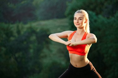 Doğa spor egzersizleri yapıyor kırmızı bir üst ve siyah pantolon içinde genç bir sarışın.