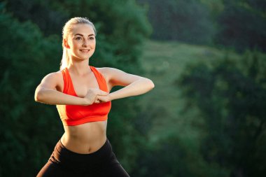 Doğa spor egzersizleri yapıyor kırmızı bir üst ve siyah pantolon içinde genç bir sarışın.