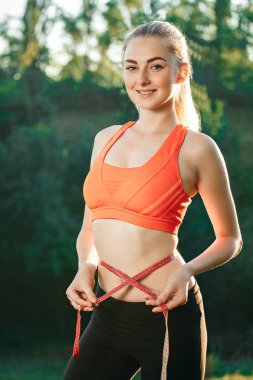 Doğada şerit cetvelle beline kırmızı üst ve siyah pantolon içinde genç bir sarışın ölçer.