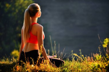 Kırmızı Top bir genç bir sarışın Fitness doğada çimlerin üzerine oturur. Bir sporcumuz jimnastik için hazırlar.