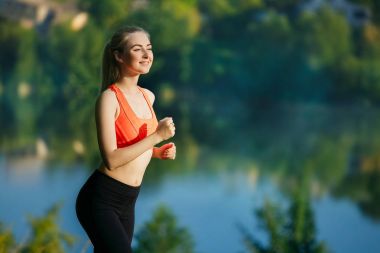 doğa üzerinde çalışan genç sarışın bir kadın. Bir kırmızı bir spor kız T-shirt Nehri yakınında park boyunca çalışır.