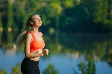 doğa üzerinde çalışan genç sarışın bir kadın. Bir kırmızı bir spor kız T-shirt Nehri yakınında park boyunca çalışır.