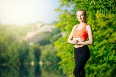 Genç sarışın kadın doğada yapıyor. Kırmızı yelek bir spor kız Nehri yakınında bir parkta duruyor