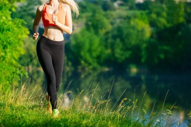 doğa üzerinde çalışan genç sarışın bir kadın. Bir kırmızı bir spor kız T-shirt Nehri yakınında park boyunca çalışır.