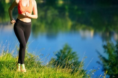doğa üzerinde çalışan genç sarışın bir kadın. Bir kırmızı bir spor kız T-shirt Nehri yakınında park boyunca çalışır.