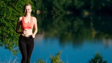 doğa üzerinde çalışan genç sarışın bir kadın. Bir kırmızı bir spor kız T-shirt Nehri yakınında park boyunca çalışır.