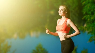 doğa üzerinde çalışan genç sarışın bir kadın. Bir kırmızı bir spor kız T-shirt Nehri yakınında park boyunca çalışır.