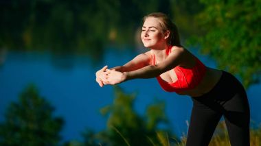 Genç sarışın kadın doğada yapıyor. Kırmızı yelek bir spor kız Nehri yakınında bir parkta duruyor