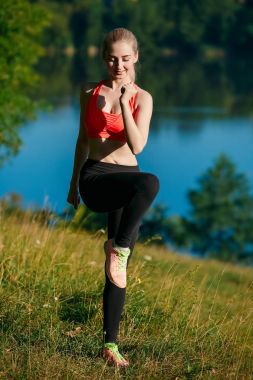 Genç sarışın kadın doğada yapıyor. Kırmızı yelek bir spor kız Nehri yakınında bir parkta duruyor