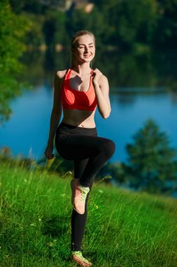 Genç sarışın kadın doğada yapıyor. Kırmızı yelek bir spor kız Nehri yakınında bir parkta duruyor