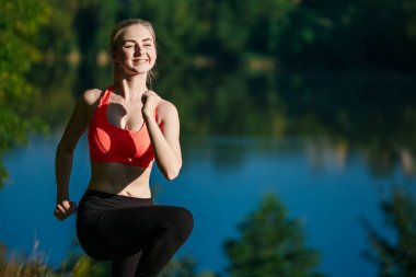 Genç sarışın kadın doğada yapıyor. Kırmızı yelek bir spor kız Nehri yakınında bir parkta duruyor
