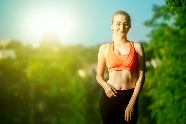 Giovane donna bionda che fa esercizi in natura. Una ragazza sportiva in gilet rosso è in piedi in un parco vicino al fiume — Foto Stock