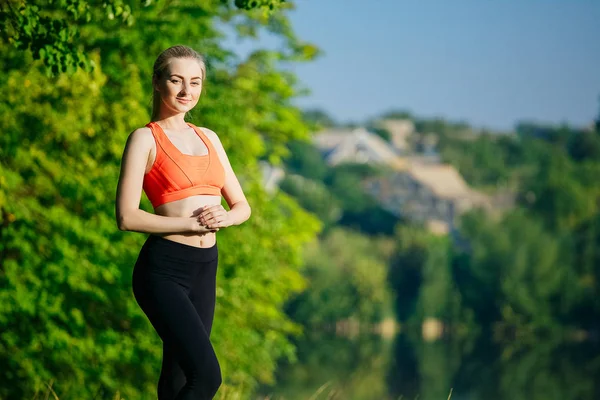 Genç sarışın kadın doğada yapıyor. Kırmızı yelek bir spor kız Nehri yakınında bir parkta duruyor