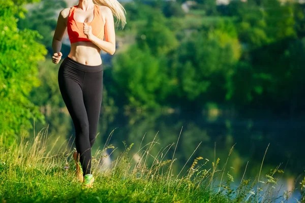 doğa üzerinde çalışan genç sarışın bir kadın. Bir kırmızı bir spor kız T-shirt Nehri yakınında park boyunca çalışır.