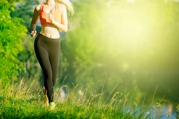 doğa üzerinde çalışan genç sarışın bir kadın. Bir kırmızı bir spor kız T-shirt Nehri yakınında park boyunca çalışır.