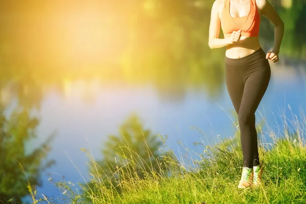 doğa üzerinde çalışan genç sarışın bir kadın. Bir kırmızı bir spor kız T-shirt Nehri yakınında park boyunca çalışır.