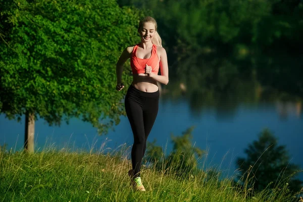 doğa üzerinde çalışan genç sarışın bir kadın. Bir kırmızı bir spor kız T-shirt Nehri yakınında park boyunca çalışır.