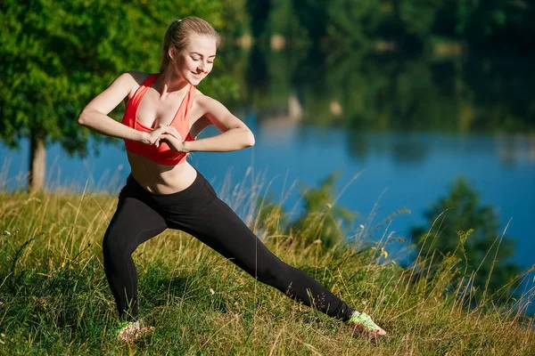 Genç sarışın kadın doğada yapıyor. Kırmızı yelek bir spor kız Nehri yakınında bir parkta duruyor
