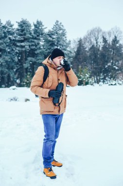 kar üzerinde duran ve bir termos ve bir fincan çay tutan bir sırt çantası ile kırmızı ceketli genç bir adam. Kış orman.
