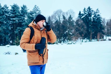 kar üzerinde duran ve bir termos ve bir fincan çay tutan bir sırt çantası ile kırmızı ceketli genç bir adam. Kış orman.