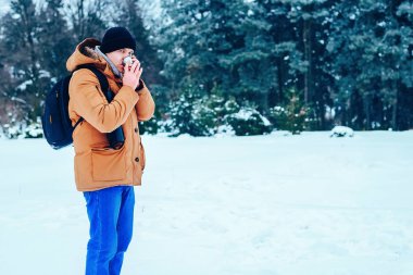 kar üzerinde duran ve bir termos ve bir fincan çay tutan bir sırt çantası ile kırmızı ceketli genç bir adam. Kış orman.
