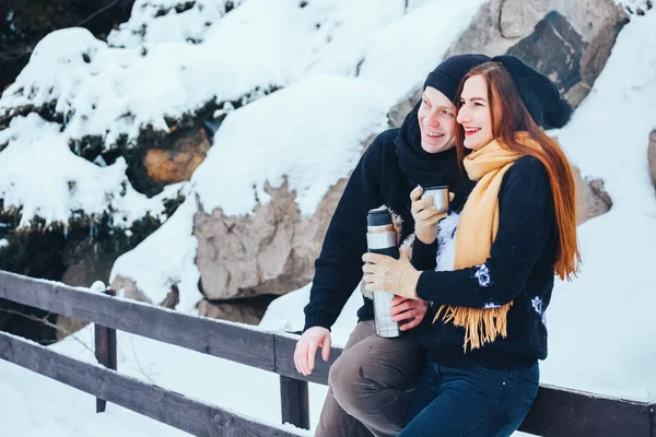 Jovem casal derrama chá quente fora de garrafa térmica na floresta de inverno — Fotografia de Stock