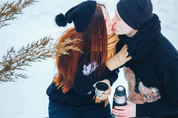 Jovem casal derrama chá quente fora de garrafa térmica na floresta de inverno — Fotografia de Stock