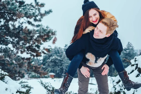 O tipo e a rapariga descansam no bosque de Inverno. Marido e mulher na neve. Jovem casal caminhando no parque de inverno. — Fotografia de Stock