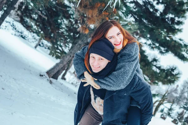 O tipo e a rapariga descansam no bosque de Inverno. Marido e mulher na neve. Jovem casal caminhando no parque de inverno. — Fotografia de Stock