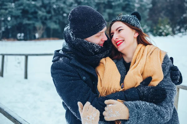 O tipo e a rapariga descansam no bosque de Inverno. Marido e mulher na neve. Jovem casal caminhando no parque de inverno. — Fotografia de Stock