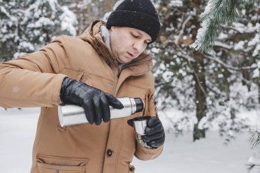 adam kış ormandaki termos bardak sıcak içecekle