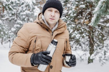 adam kış ormandaki termos bardak sıcak içecekle