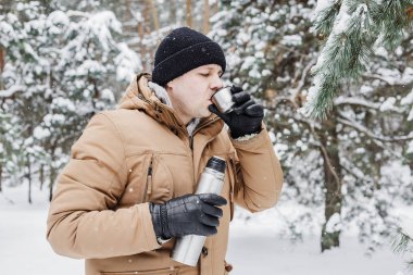 adam kış ormandaki termos bardak sıcak içecekle