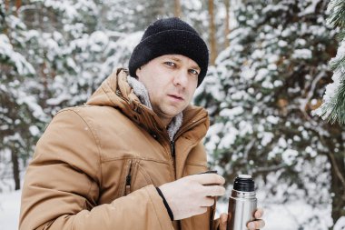 adam kış ormandaki termos bardak sıcak içecekle