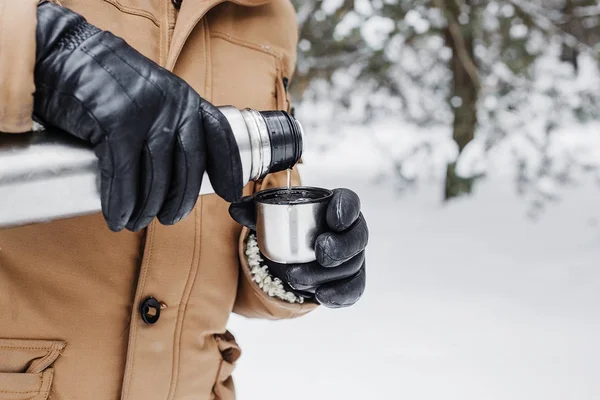 man with hot drink in thermos cup in winter forest