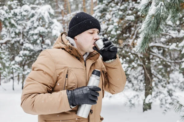 adam kış ormandaki termos bardak sıcak içecekle