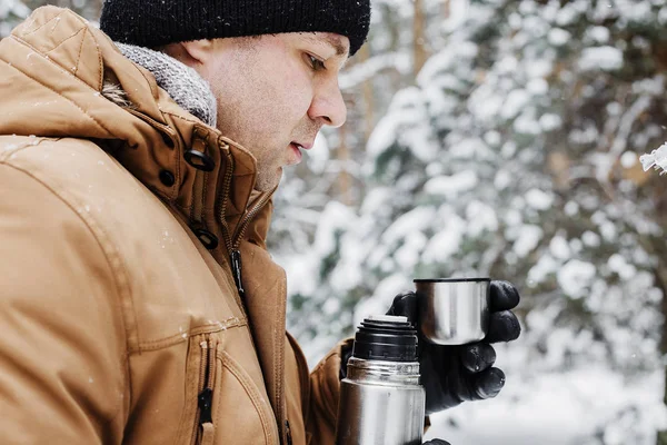 adam kış ormandaki termos bardak sıcak içecekle