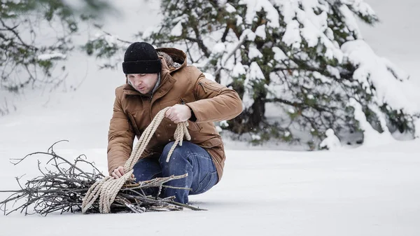 çırpı ve kış ormanın içinde bir ip ile kırmızı bir ceket bir adam. Yakacak odun adam toplar