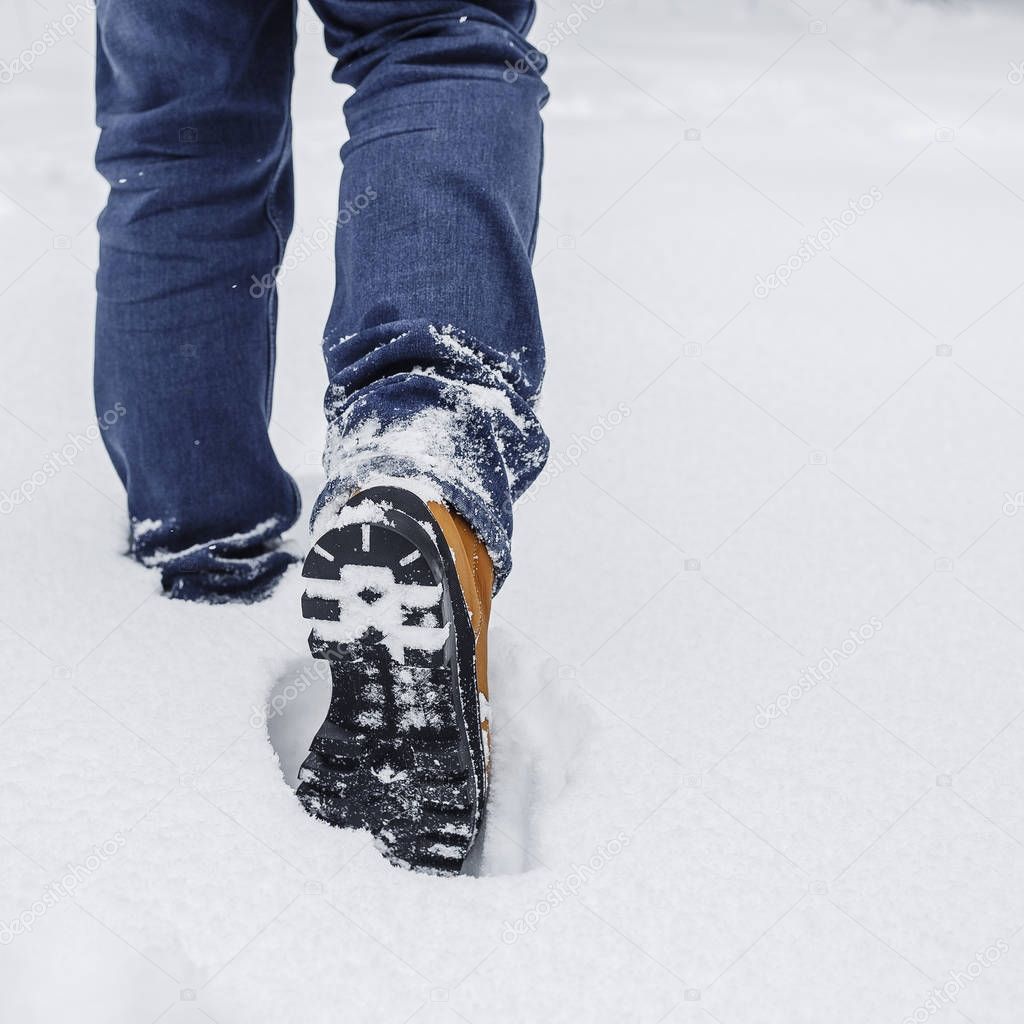 close-up of male legs in winter shoes and blue jeans walking on snow.