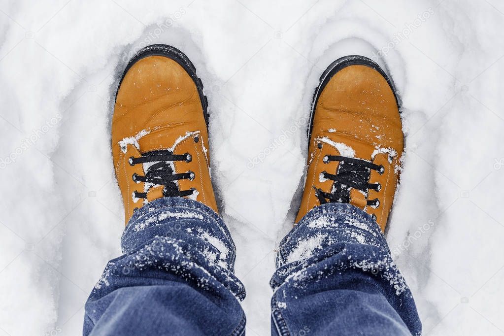 close-up of male legs in blue jeans and winter shoes on snow