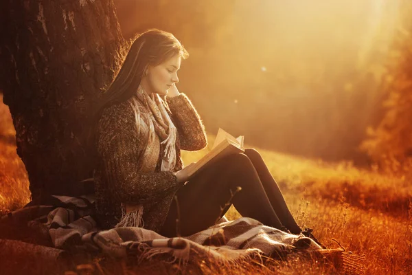 Красивая юная брюнетка сидит на опавших осенних листьях в парке, читает книгу — стоковое фото