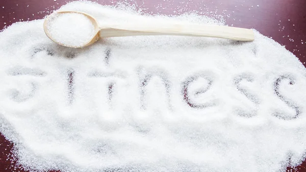 The word FITNESS written on a covered sugar and a wooden spoon on the table. — Stock Photo, Image
