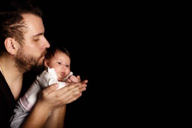 Siyah tişörtlü yakışıklı kaslı adamın stüdyo portresi. Siyah arka planlı şirin bir bebeğin ellerinde. Aile, aşk ve mutluluk kavramı.