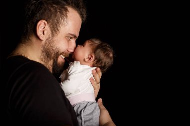 Siyah tişörtlü yakışıklı kaslı adamın stüdyo portresi. Siyah arka planlı şirin bir bebeğin ellerinde. Aile, aşk ve mutluluk kavramı.