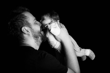 Siyah tişörtlü yakışıklı kaslı adamın stüdyo portresi. Siyah arka planlı şirin bir bebeğin ellerinde. Aile, aşk ve mutluluk kavramı.